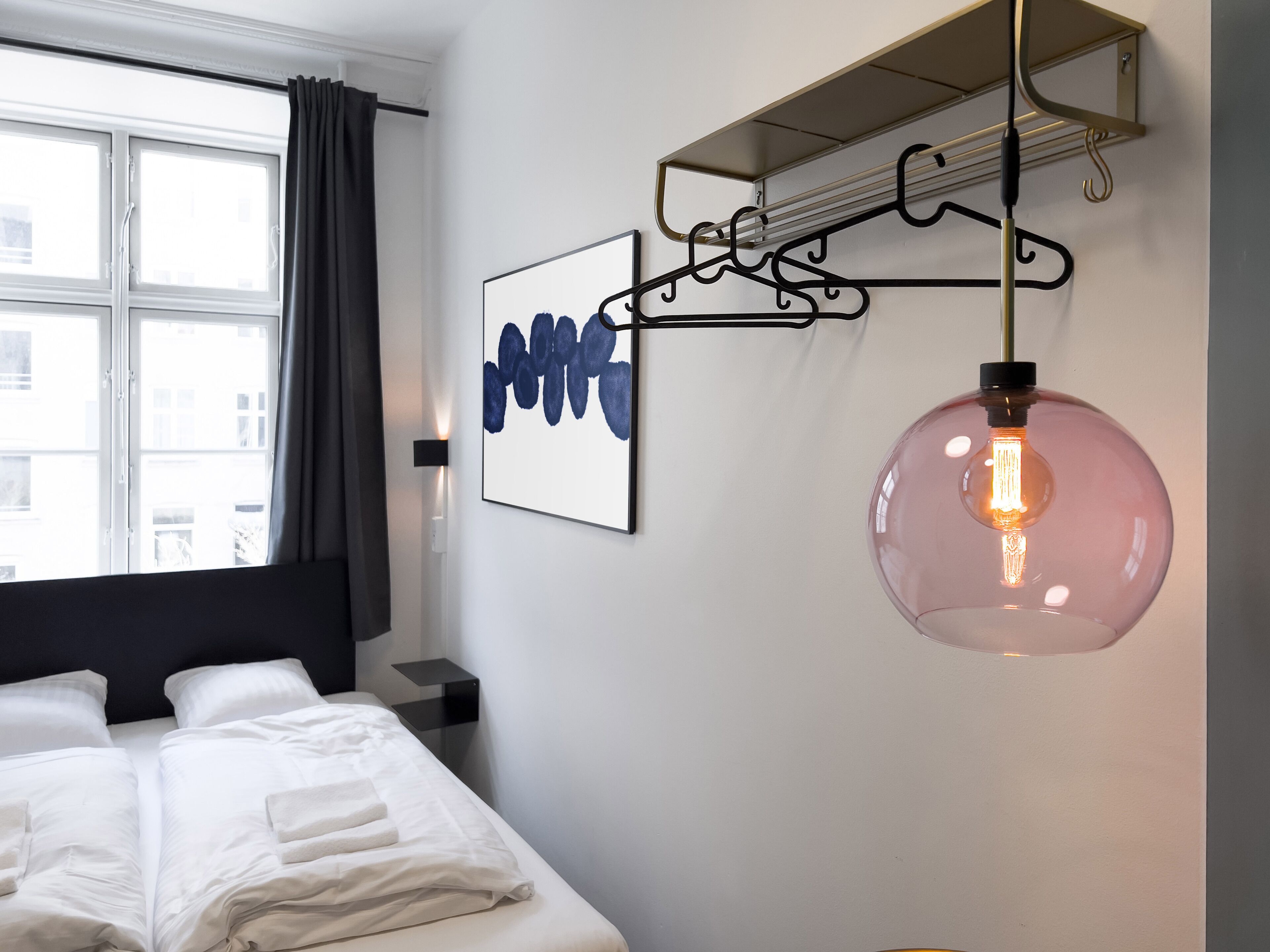A modern hotel room with a large bed, a wall-mounted light fixture, and a framed artwork.