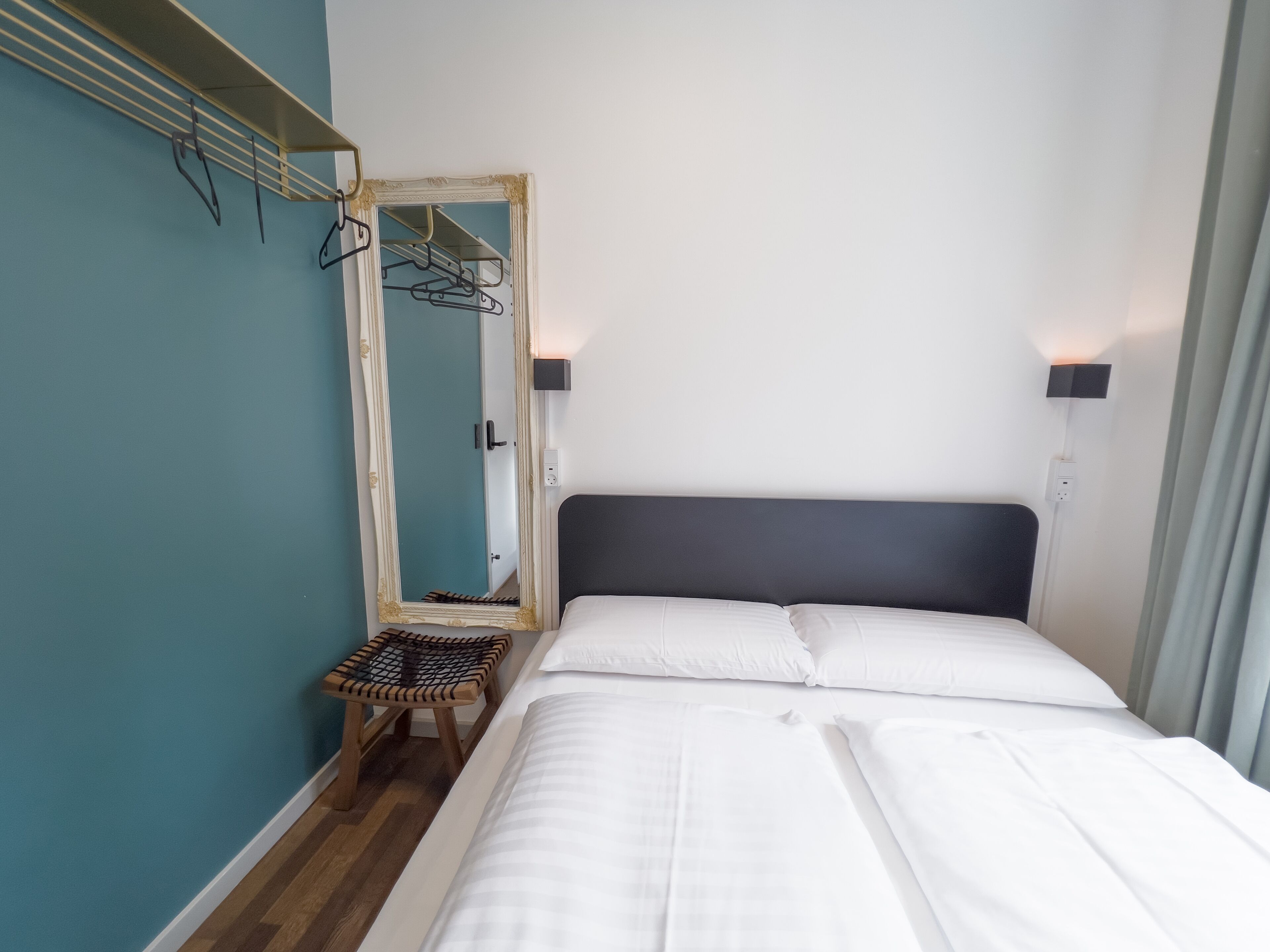 Een slaapkamer met een bed, een spiegel, een kledingrek en een klein tafeltje.