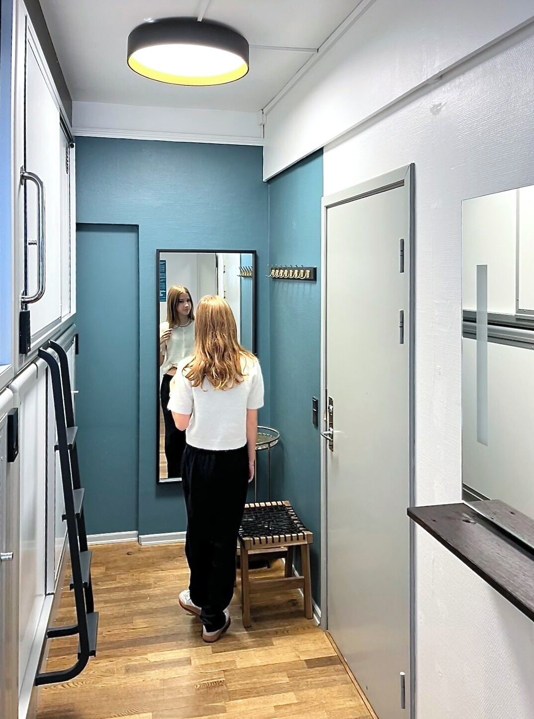 Un pasillo estrecho con una pared azul, un banco de madera y una puerta con espejo.