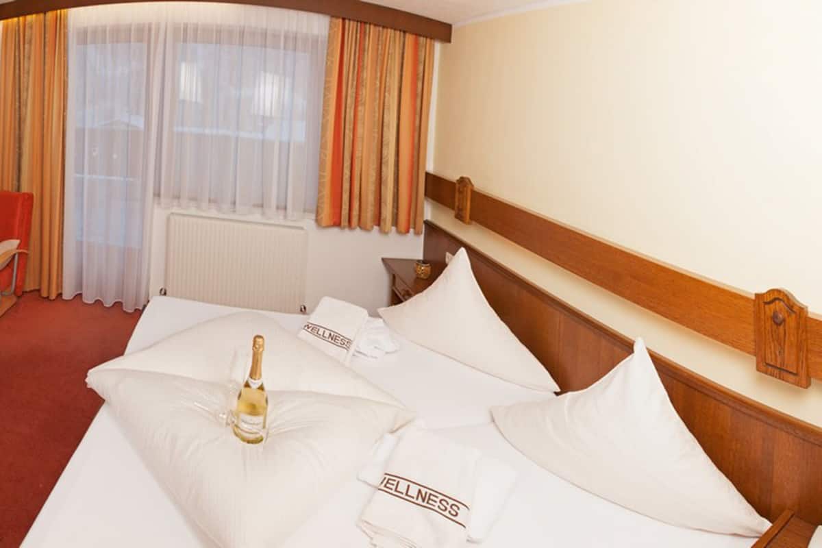 Una camera d'albergo con un letto, una poltrona rossa, un tavolino con un vaso e un libro, e una TV a parete.