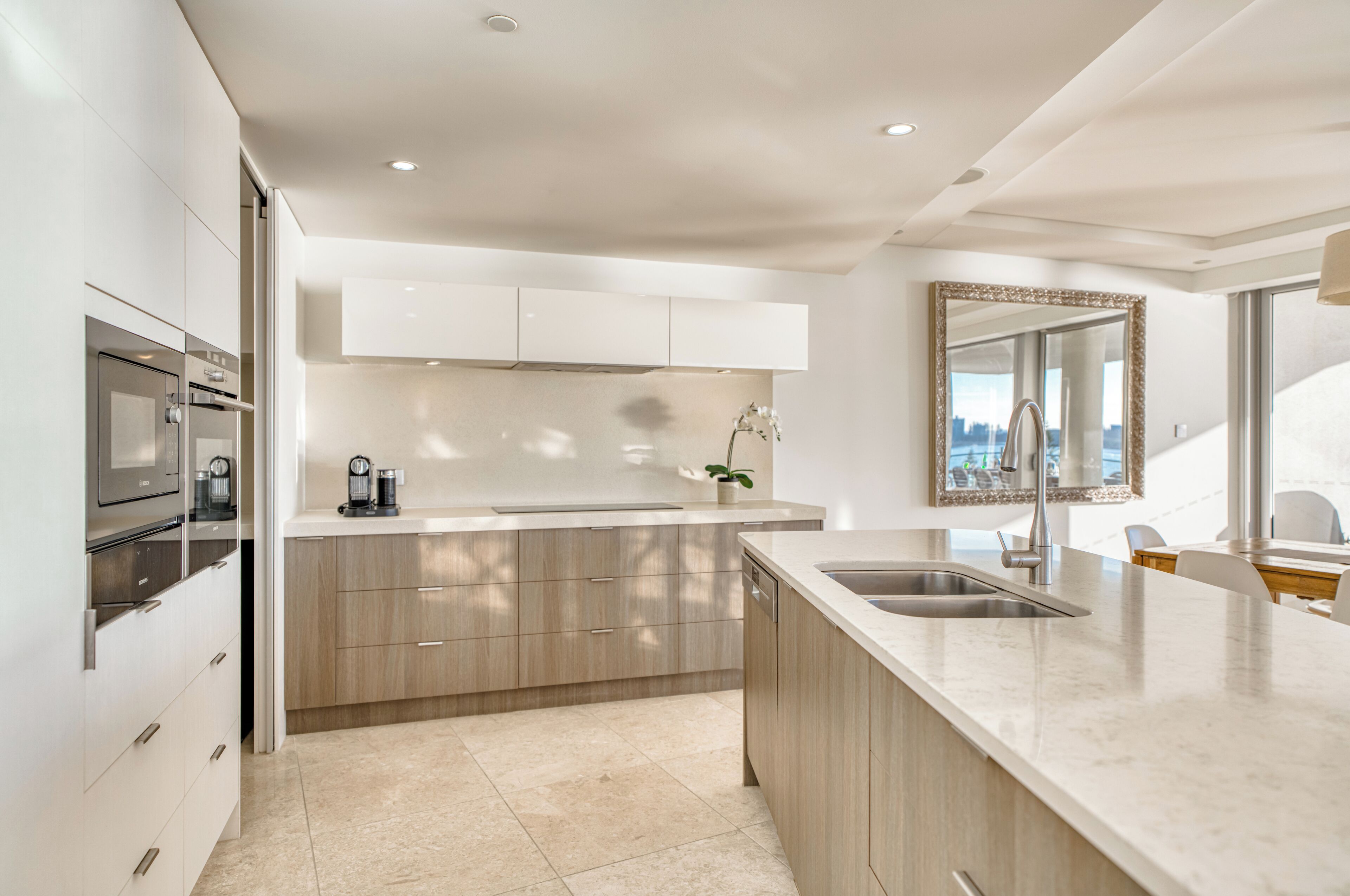 A modern kitchen with a central island, built-in oven, and a large mirror above the sink.