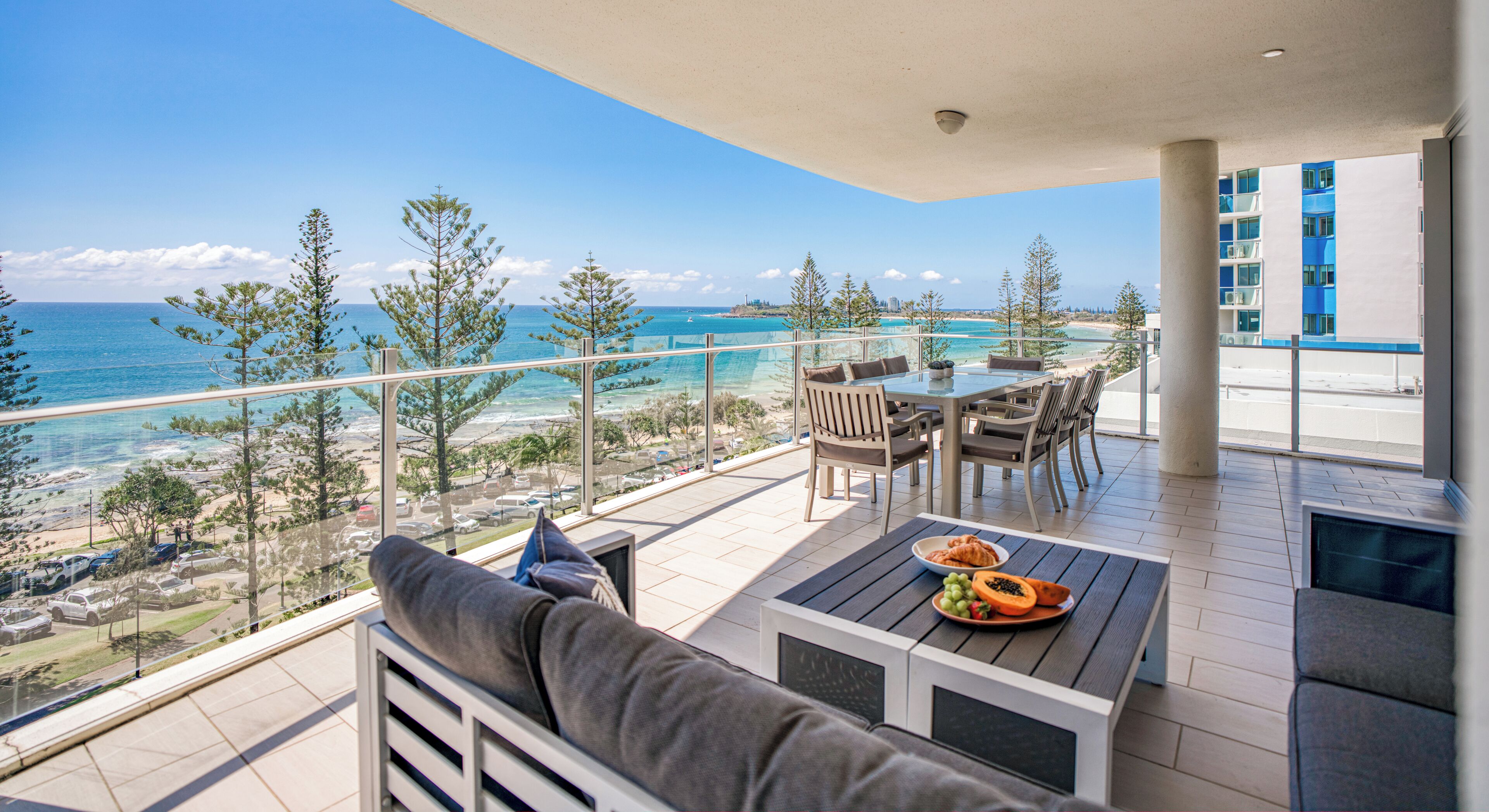 A balcony with a view of the beach and ocean, furnished with a table, chairs, and a sofa.