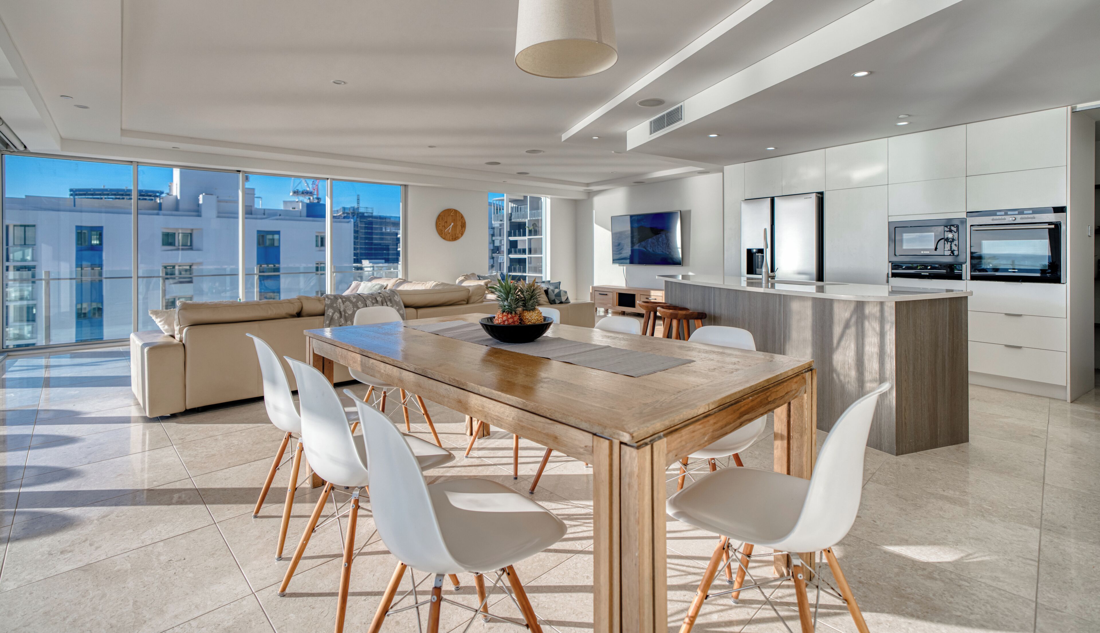 A modern kitchen with a wooden dining table, white chairs, and a large island.