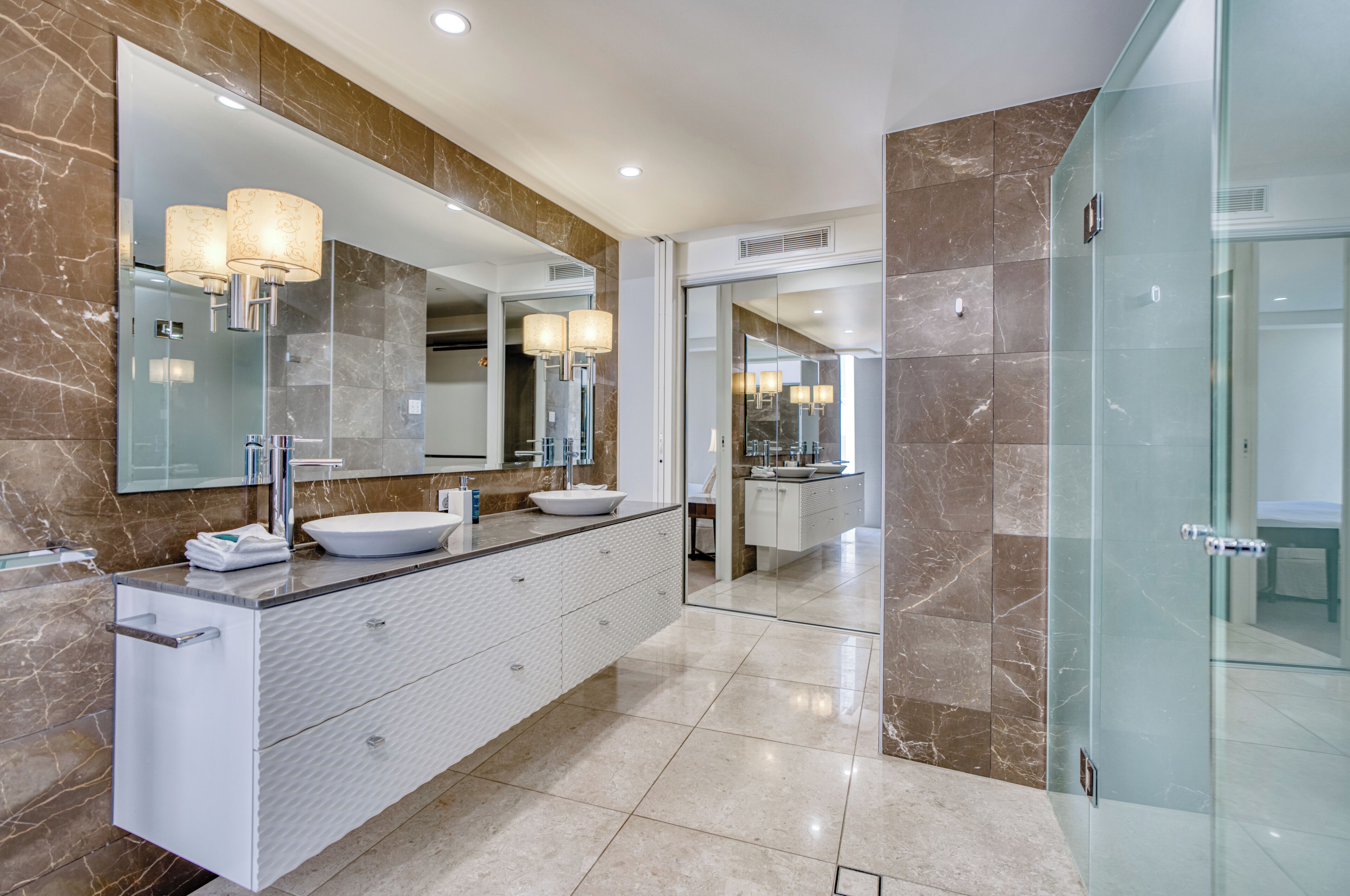 A modern bathroom with a large mirror, two sinks, and a glass shower enclosure.