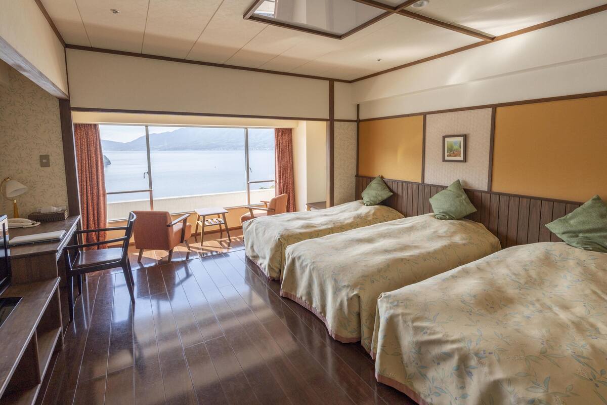 Een hotelkamer met twee bedden, een bureau, een stoel en uitzicht op zee.