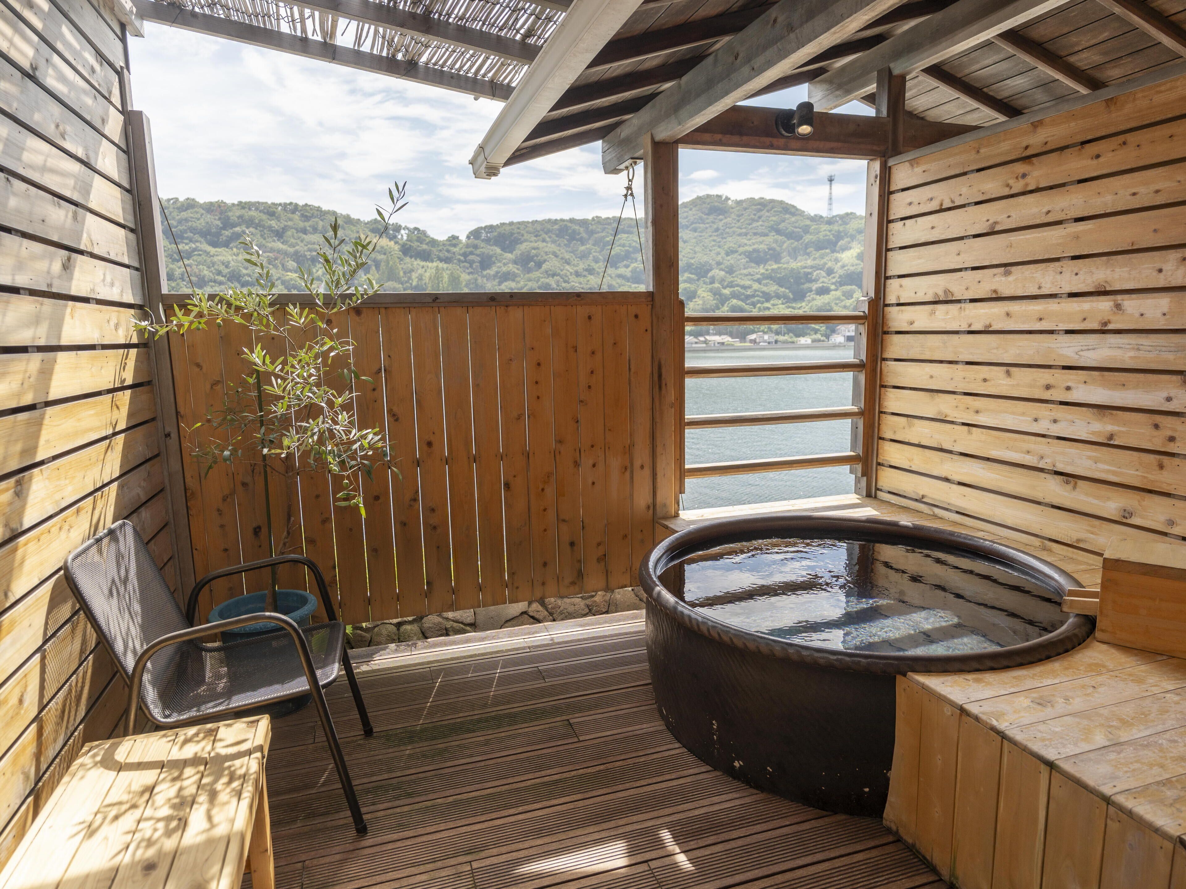 A wooden spa area with a hot tub, a chair, and a view of a lake.