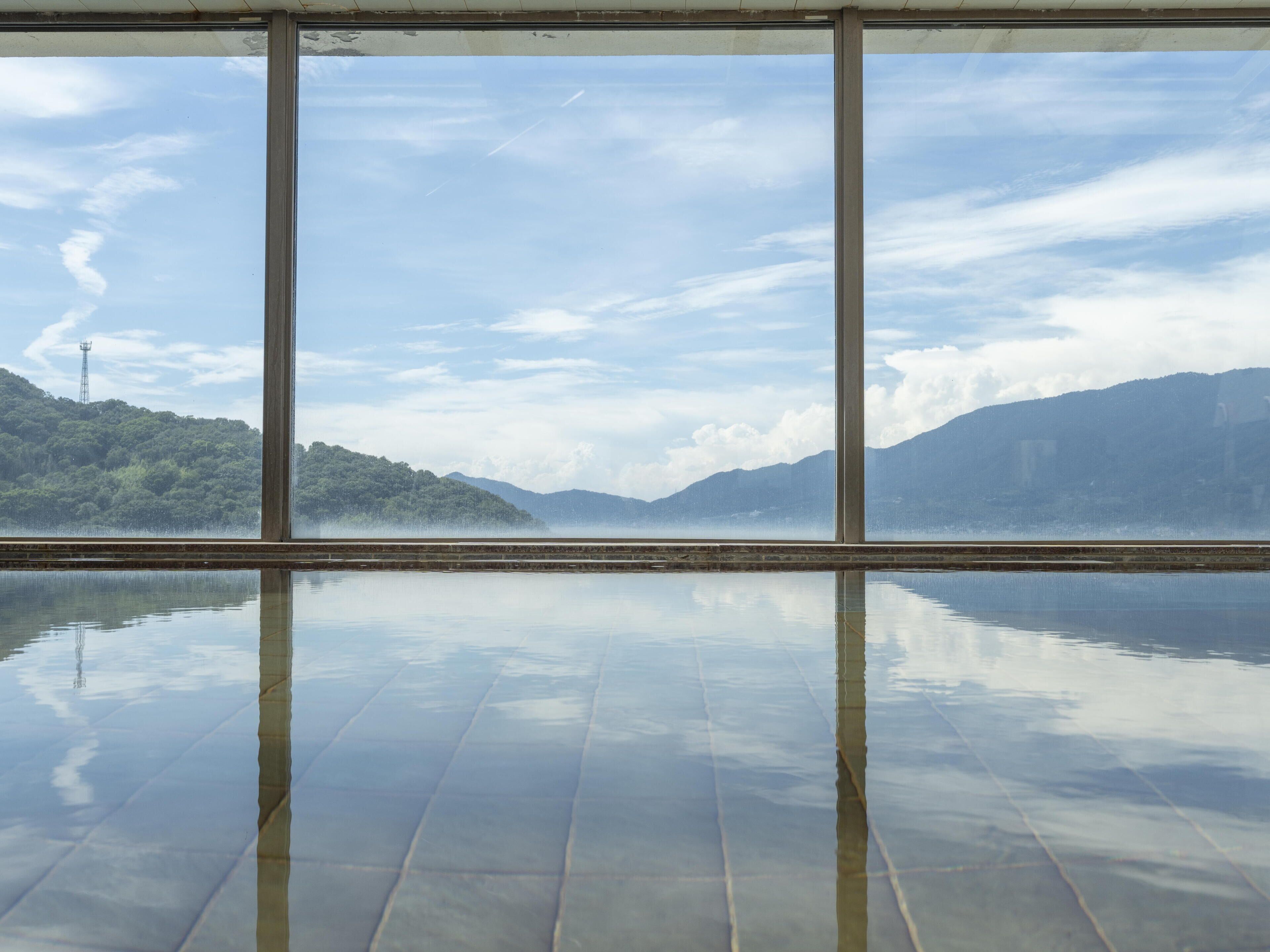 Vista a través de amplios ventanales de una masa de agua tranquila que refleja el cielo y el paisaje circundante.