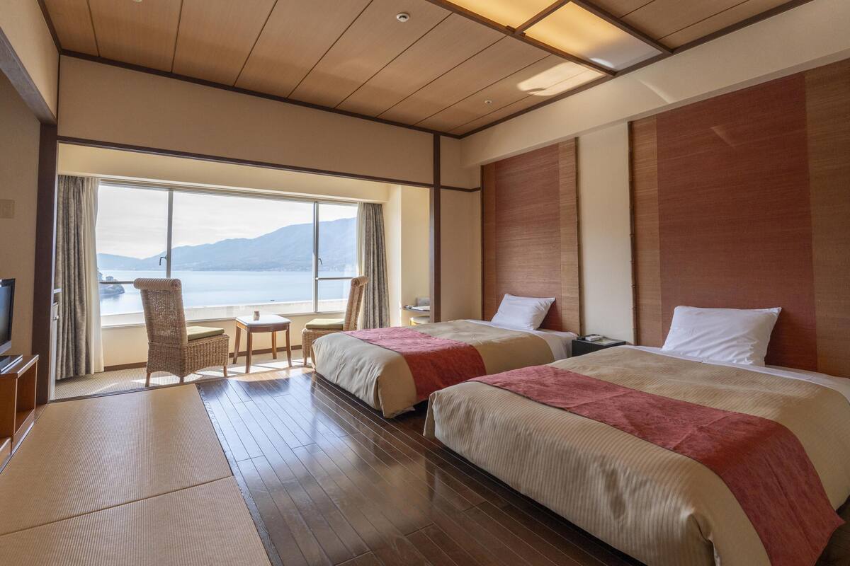 Een hotelkamer met twee bedden, een televisie, een klein tafeltje en uitzicht op zee.