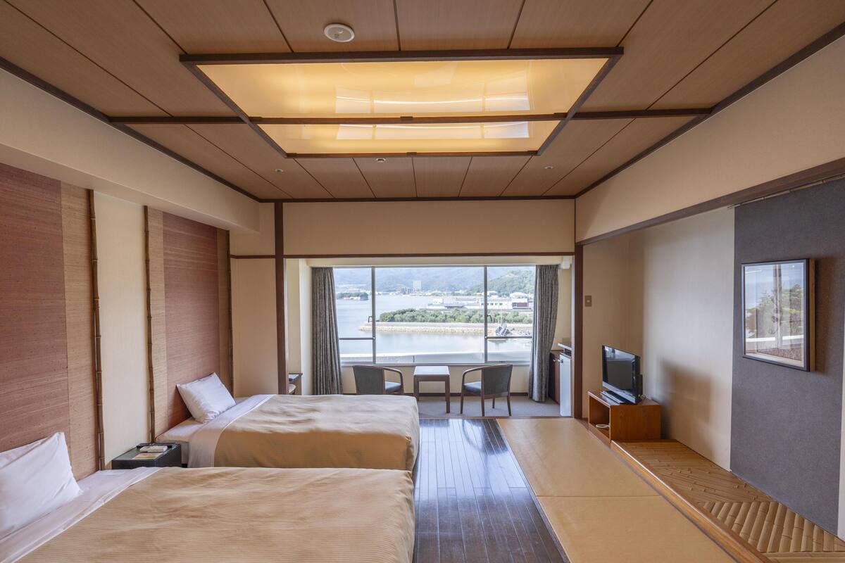 Een hotelkamer met twee bedden, een televisie, een bureau en een groot raam met uitzicht op de stad.