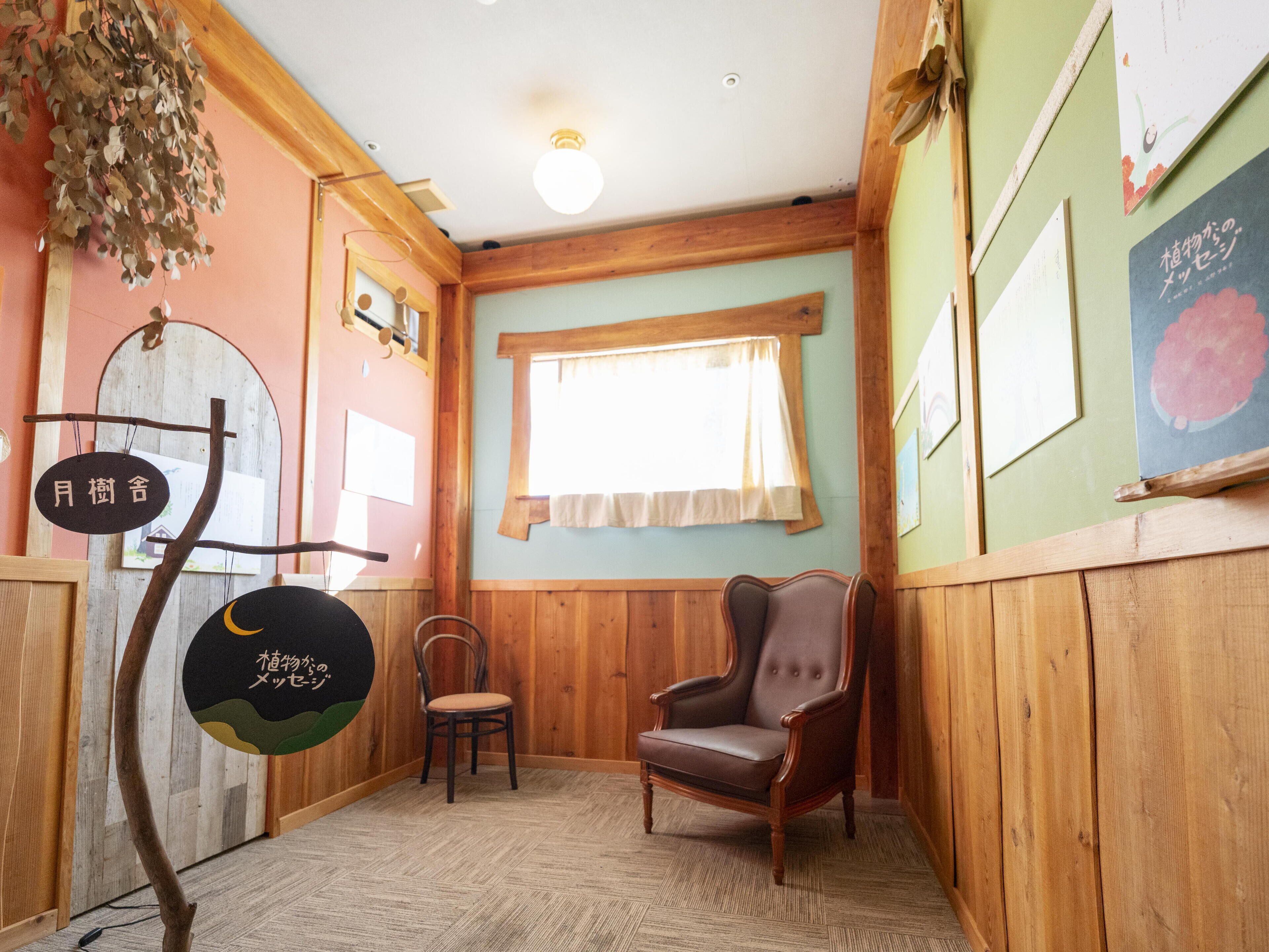 A room with wooden walls, a wooden chair, a small table, and a window with curtains.