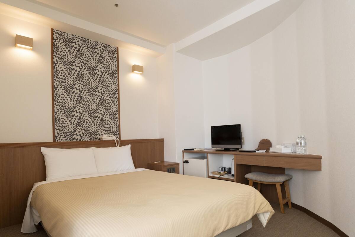 Hotelkamer met een bed, een bureau met een computer, een stoel en een kleine koelkast.