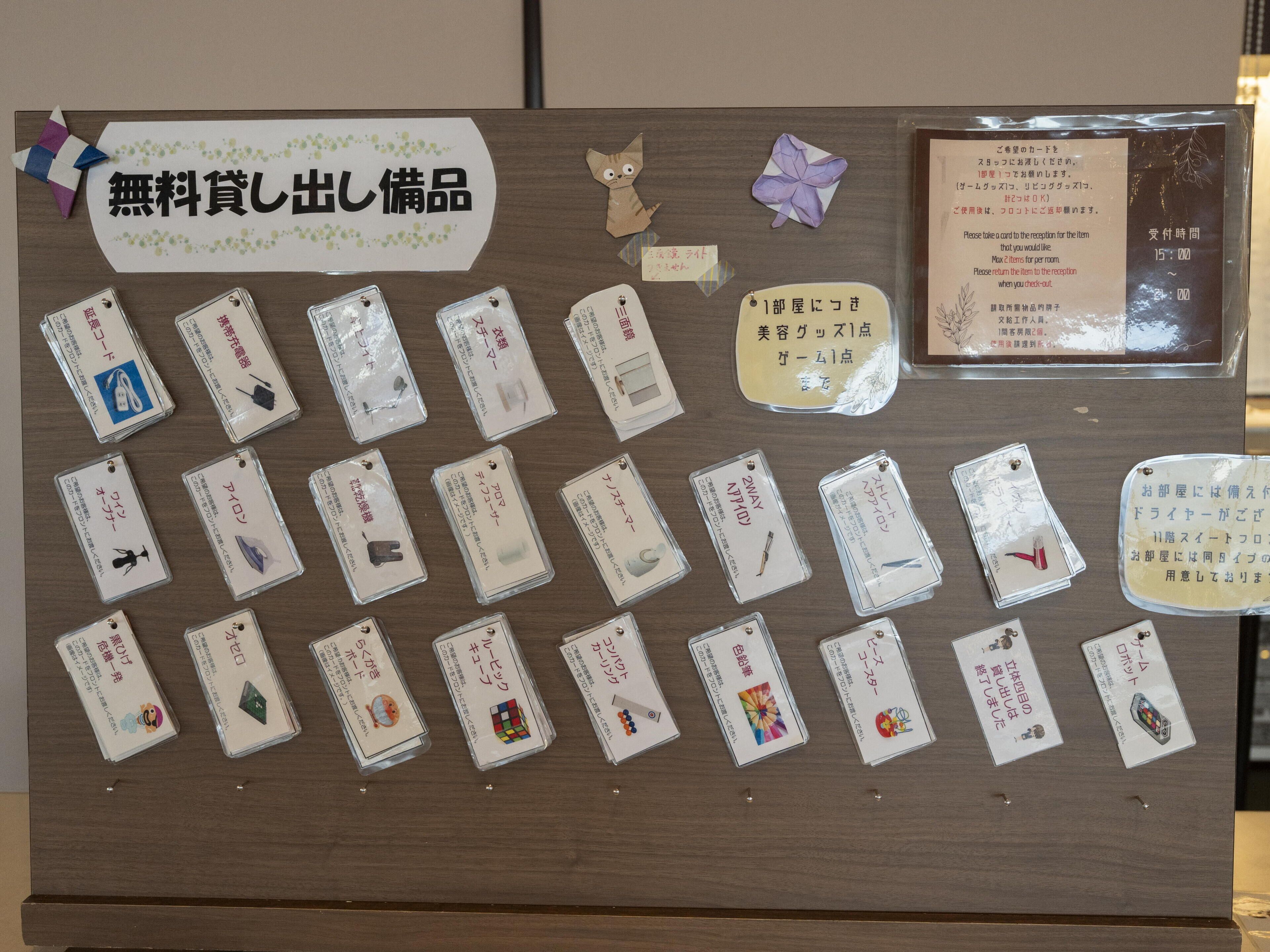 Un panel de exhibición con varios objetos etiquetados en japonés, incluyendo un letrero de artículos gratuitos y una tarjeta con instrucciones.