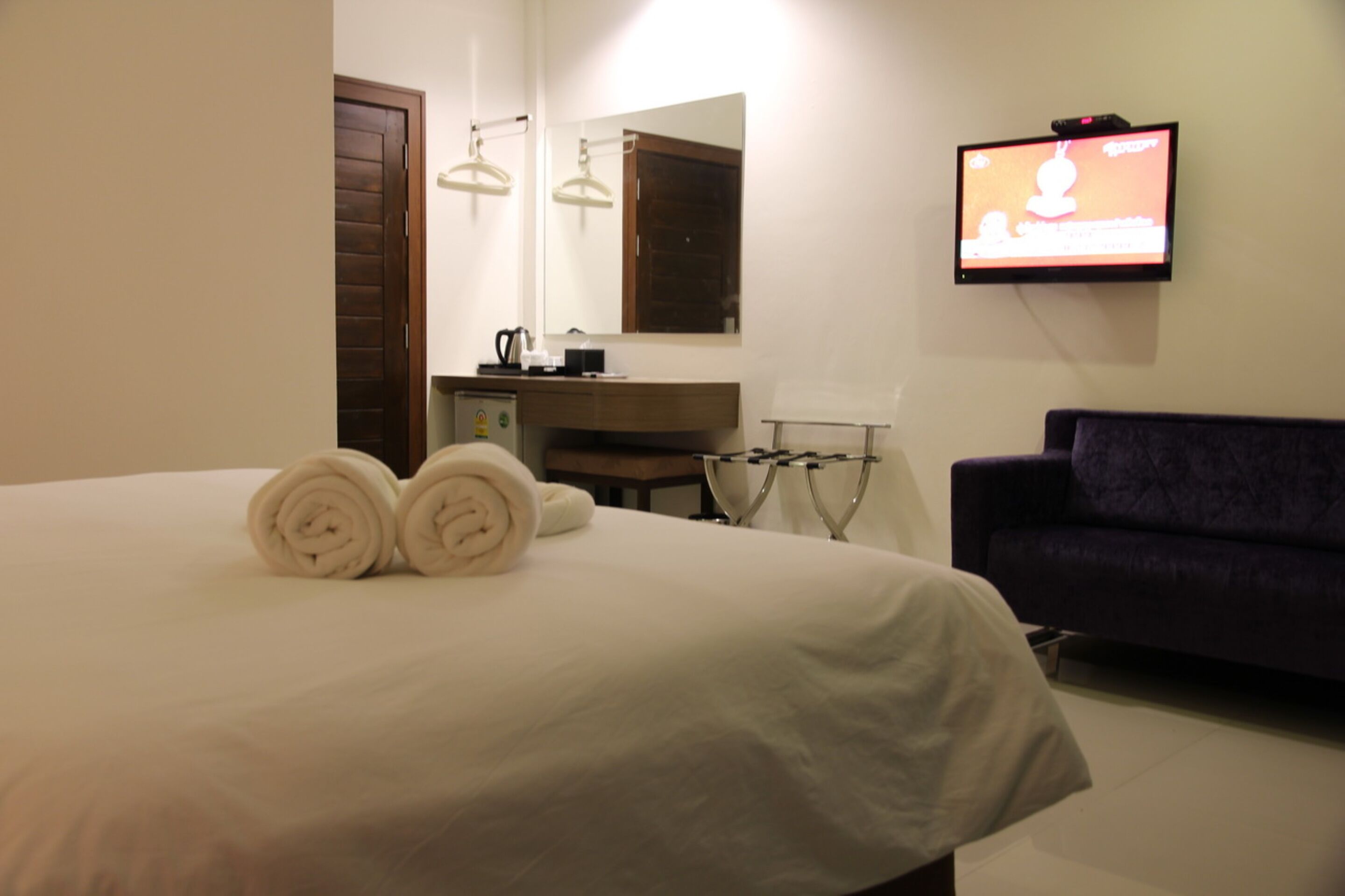 Ein Hotelzimmer mit einem Bett, einem an der Wand montierten Fernseher, einem dunkelgrauen Sofa und einer Holztür.