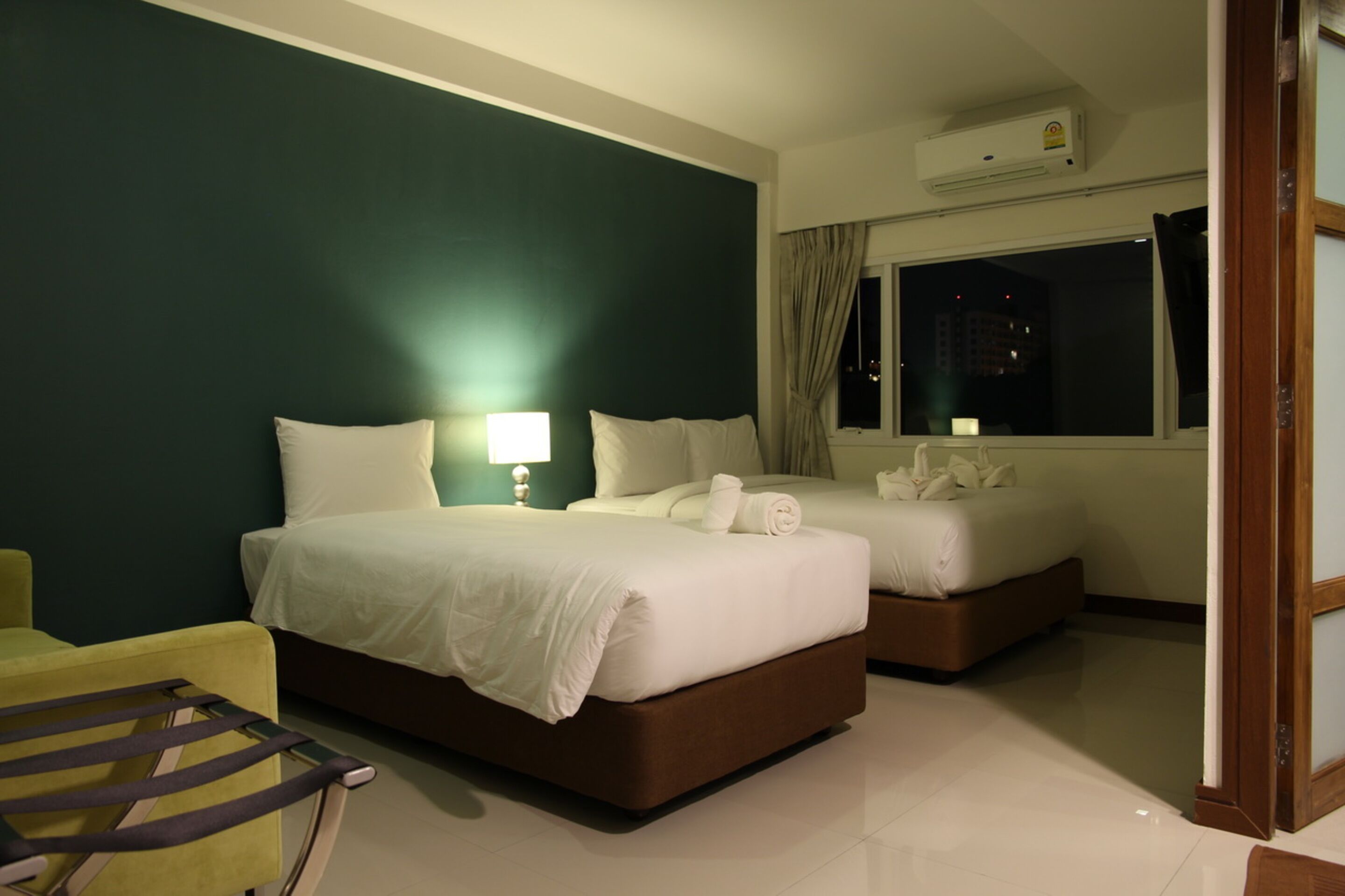 Een hotelkamer met twee bedden, een nachtkastje, een lamp en uitzicht op de stad 's nachts.