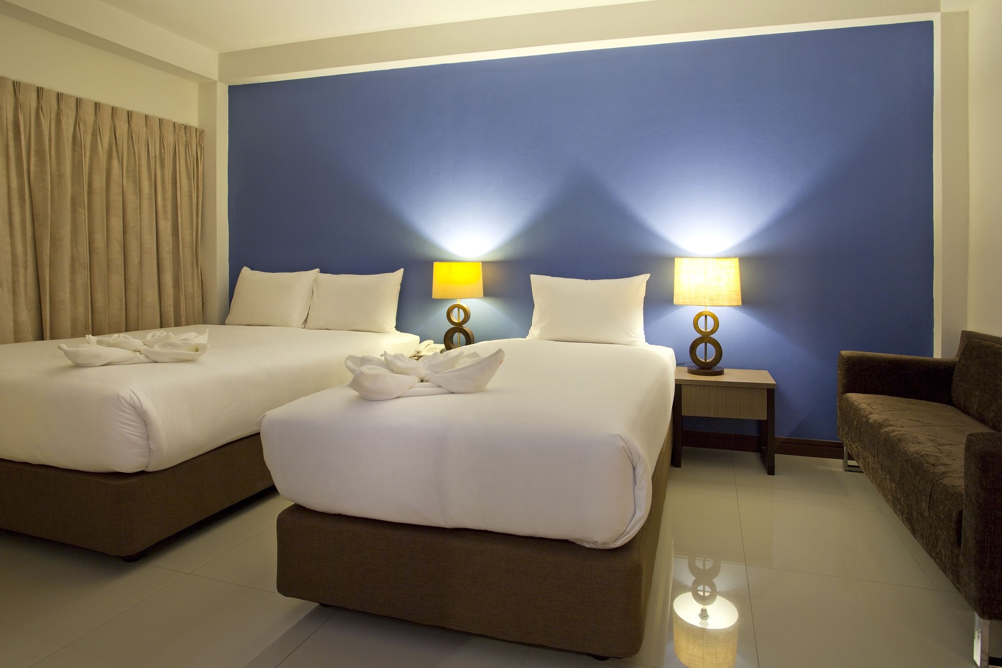 A hotel room with two beds, a sofa, and two bedside tables with lamps.