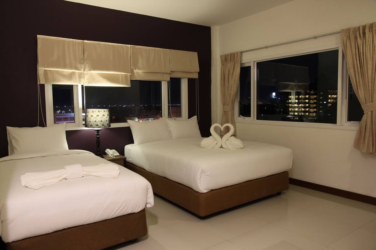 A hotel room with two beds, a nightstand with a lamp, and a view of the city at night.