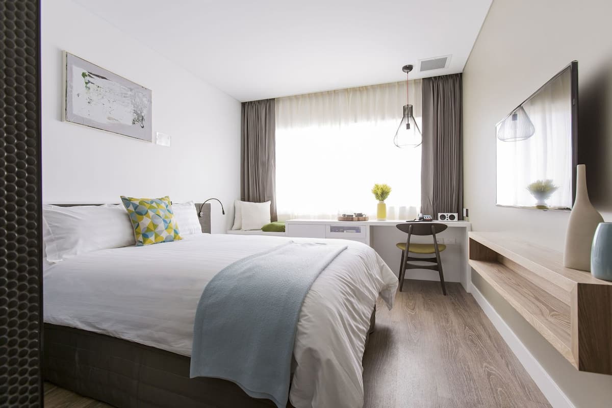 Una habitación de hotel moderna con cama, escritorio, silla y un ventanal con cortinas.