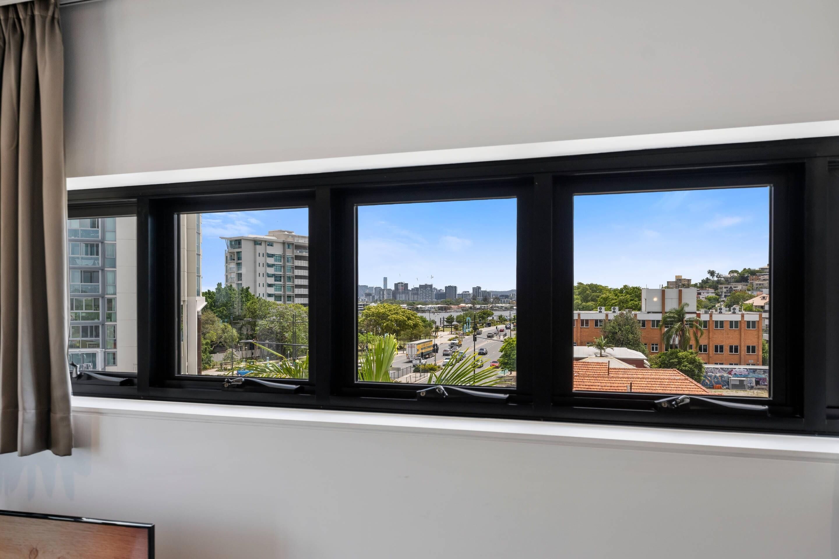 A room with a large window overlooking a cityscape, including buildings and greenery.