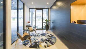 A modern reception area with a round, patterned rug, a reception desk, and a potted plant. - The Kingsford, an Ascend Collection Hotel (Hamilton)
