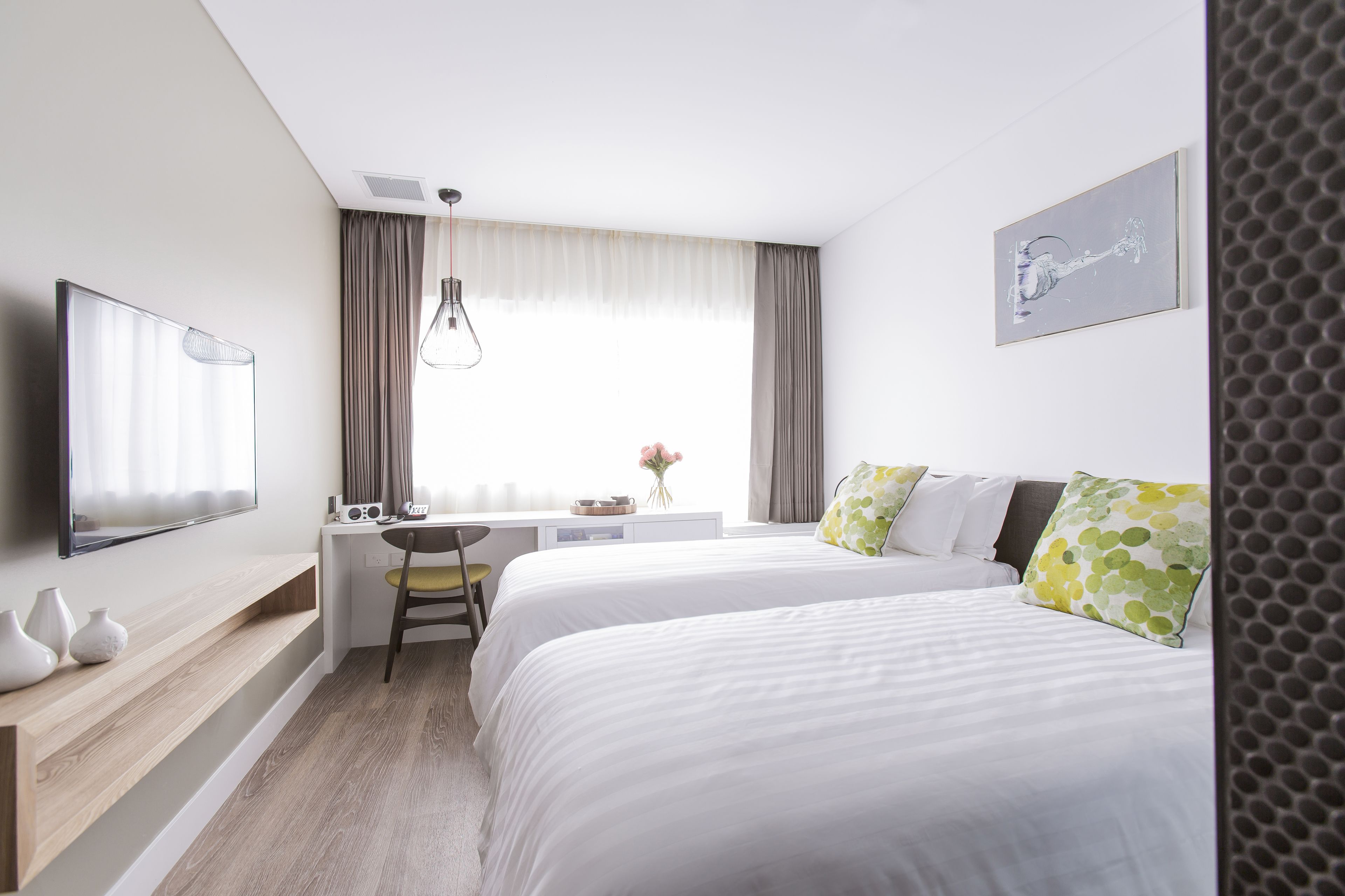 Una habitación de hotel con cama, escritorio, silla, televisor y ventana con cortinas.