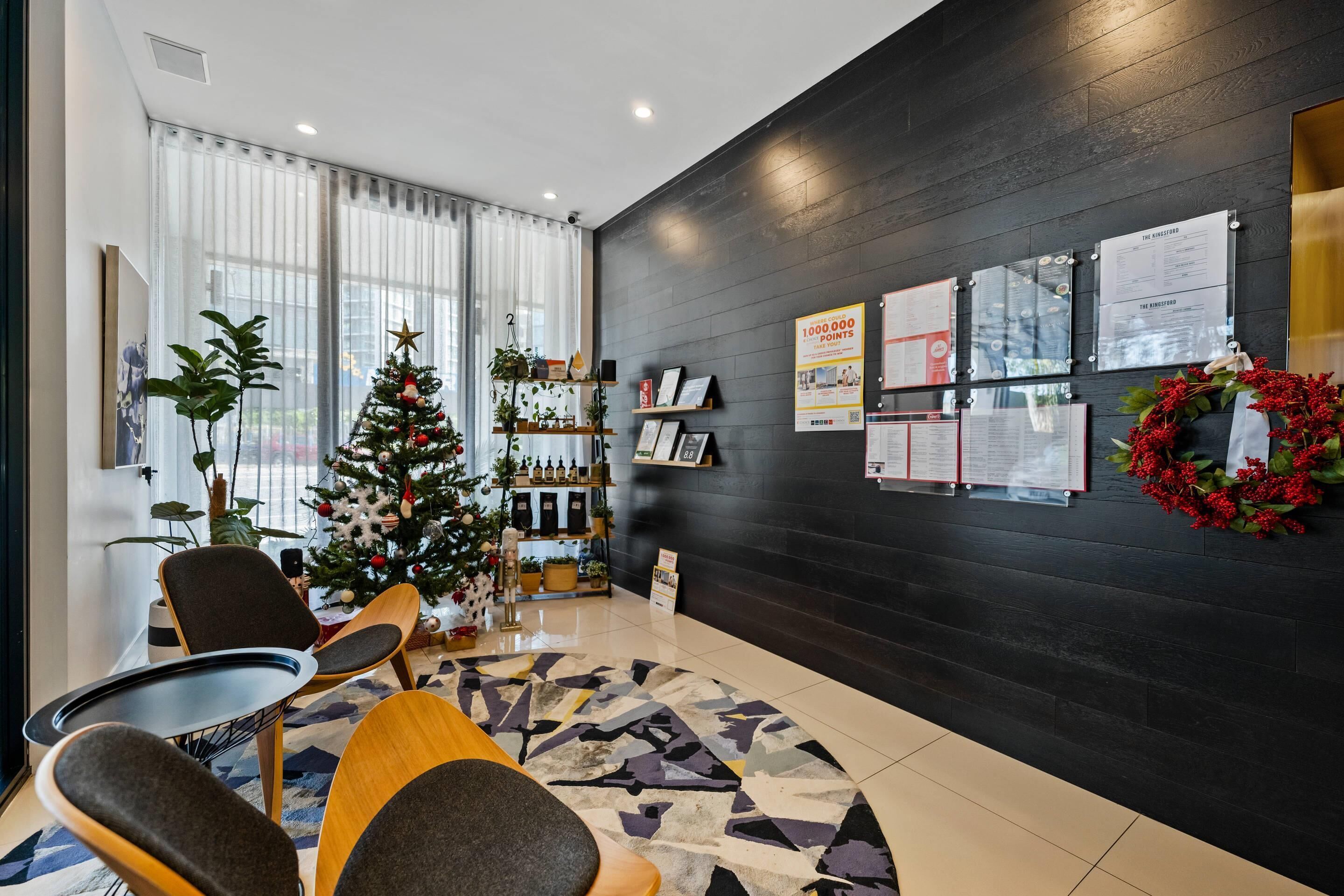 A modern hotel lobby with a Christmas tree, seating area, and wall-mounted information boards.