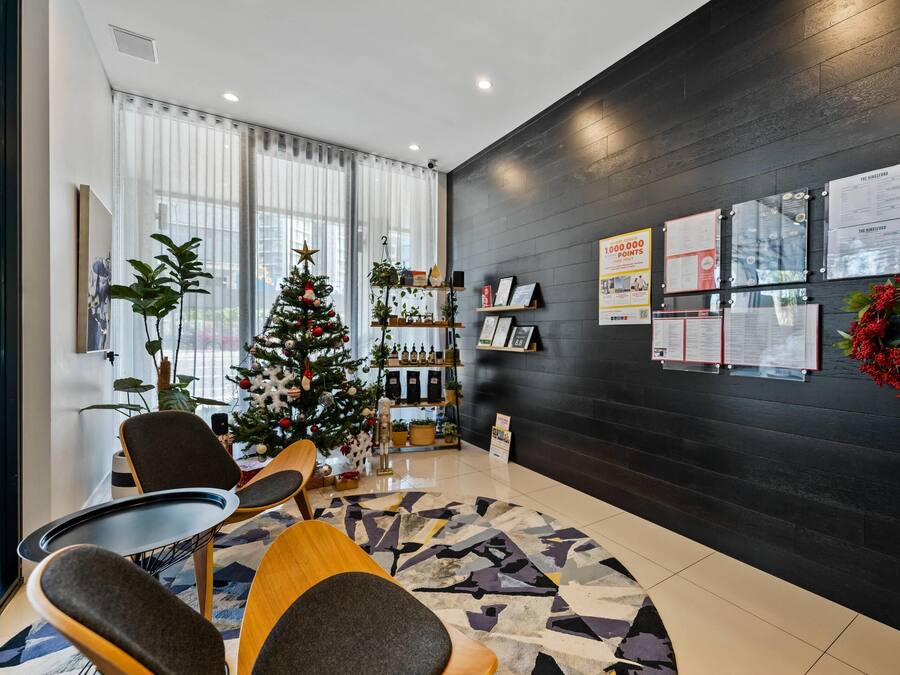 A modern hotel lobby with a Christmas tree, seating area, and wall-mounted information boards.