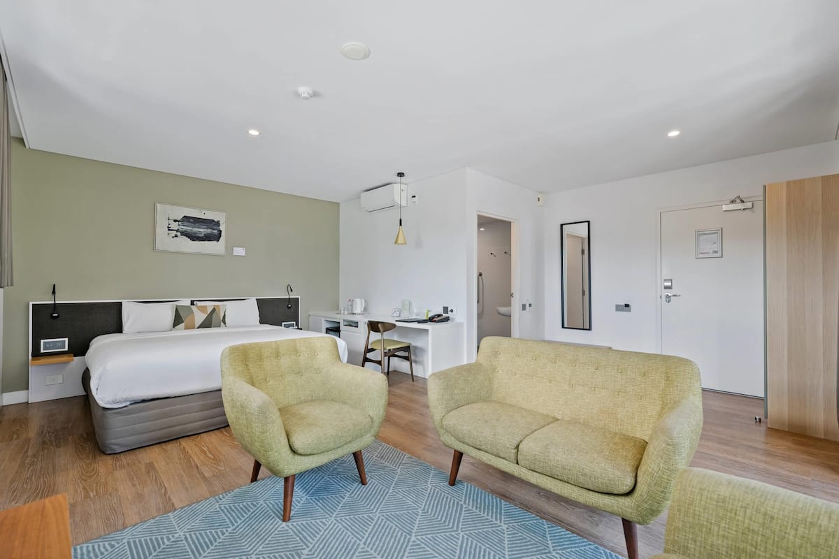 Una habitación de hotel moderna con una cama, dos sillones, un escritorio y una pequeña kitchenette.