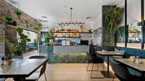 A modern restaurant interior with brick walls, hanging plants, a herringbone-patterned backsplash, and a bar area. - The Kingsford, an Ascend Collection Hotel (Hamilton)