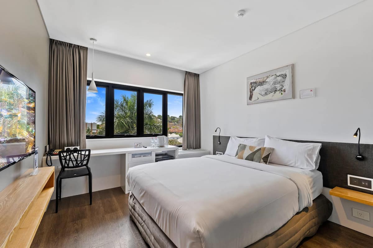 Habitación de hotel moderna con una cama grande, un escritorio con silla, una ventana con cortinas y una obra de arte colgada.