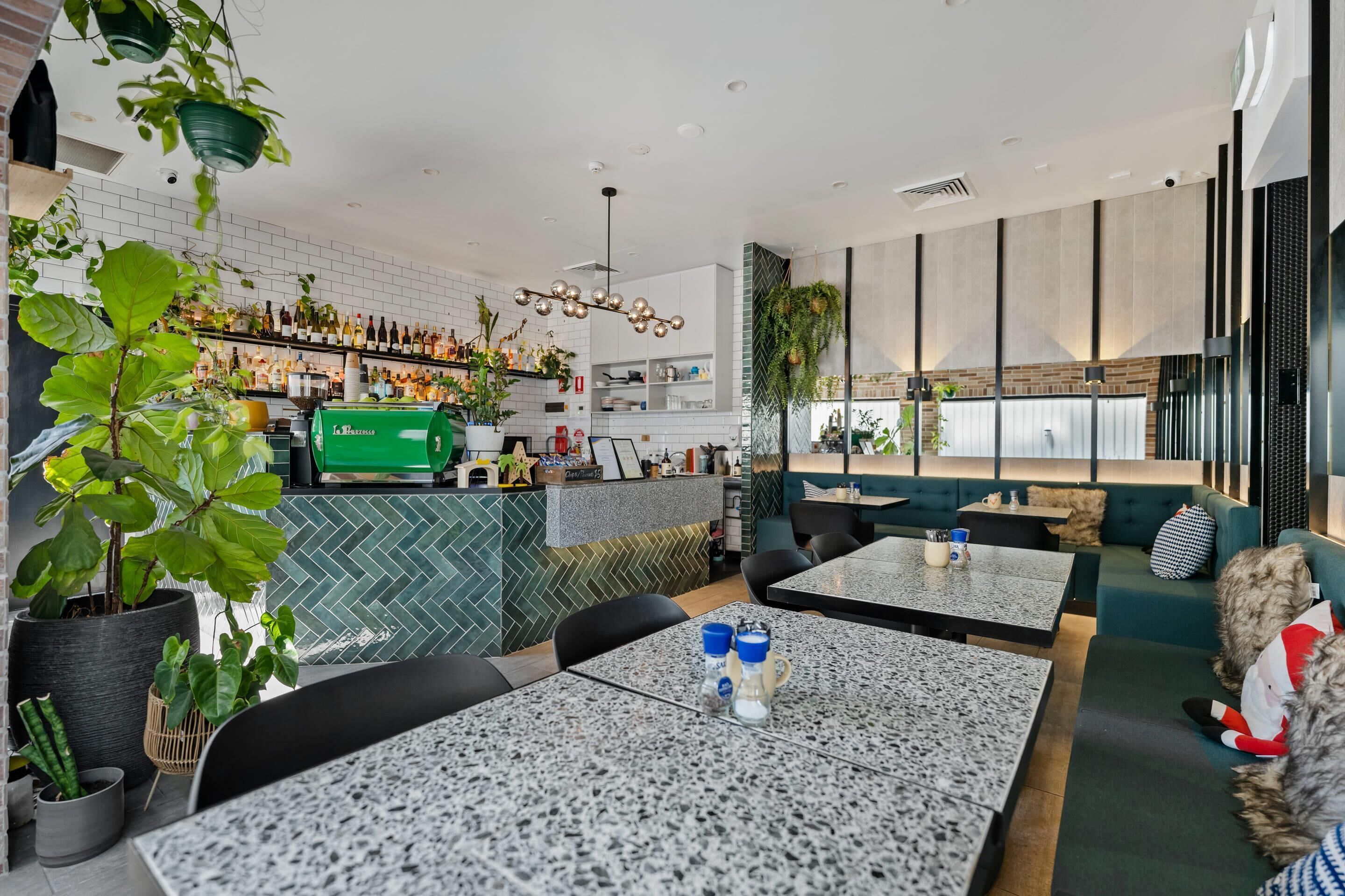 A modern restaurant with a bar area, seating, and potted plants.