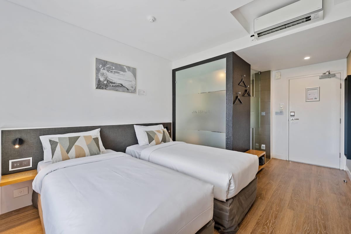 Habitación de hotel con dos camas, un espejo grande, un armario y un aire acondicionado de pared.