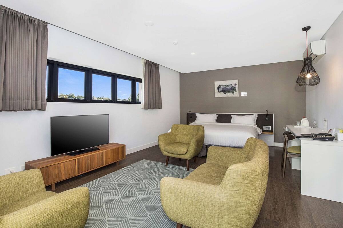Una habitación de hotel moderna con una cama grande, un televisor, un escritorio y dos sillones.