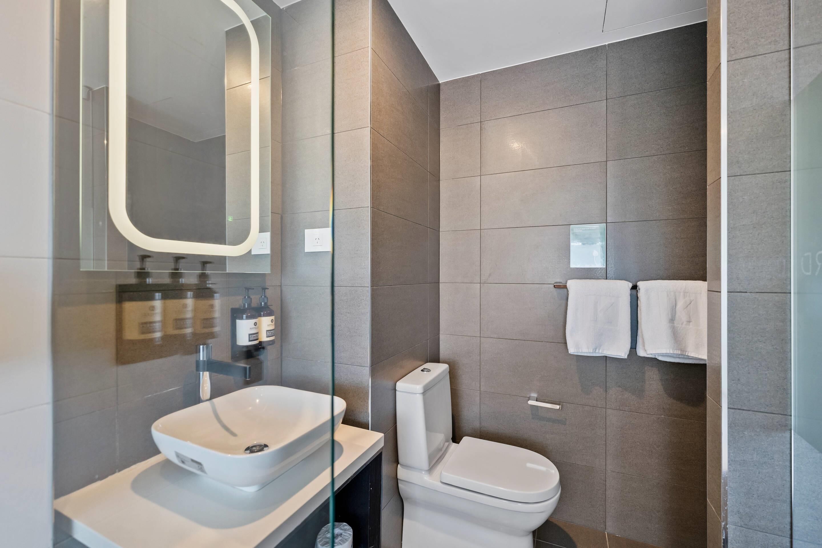 A modern bathroom with a large mirror, a white sink, and a toilet.