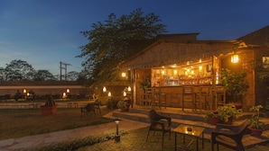 An outdoor bar area with seating and tables, surrounded by potted plants and a wooden building. - Green Park Chitwan (Sauraha)