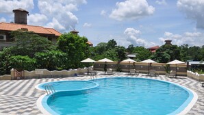 A swimming pool with a checkered tile deck, lounge chairs, and umbrellas. - Green Park Chitwan (Sauraha)