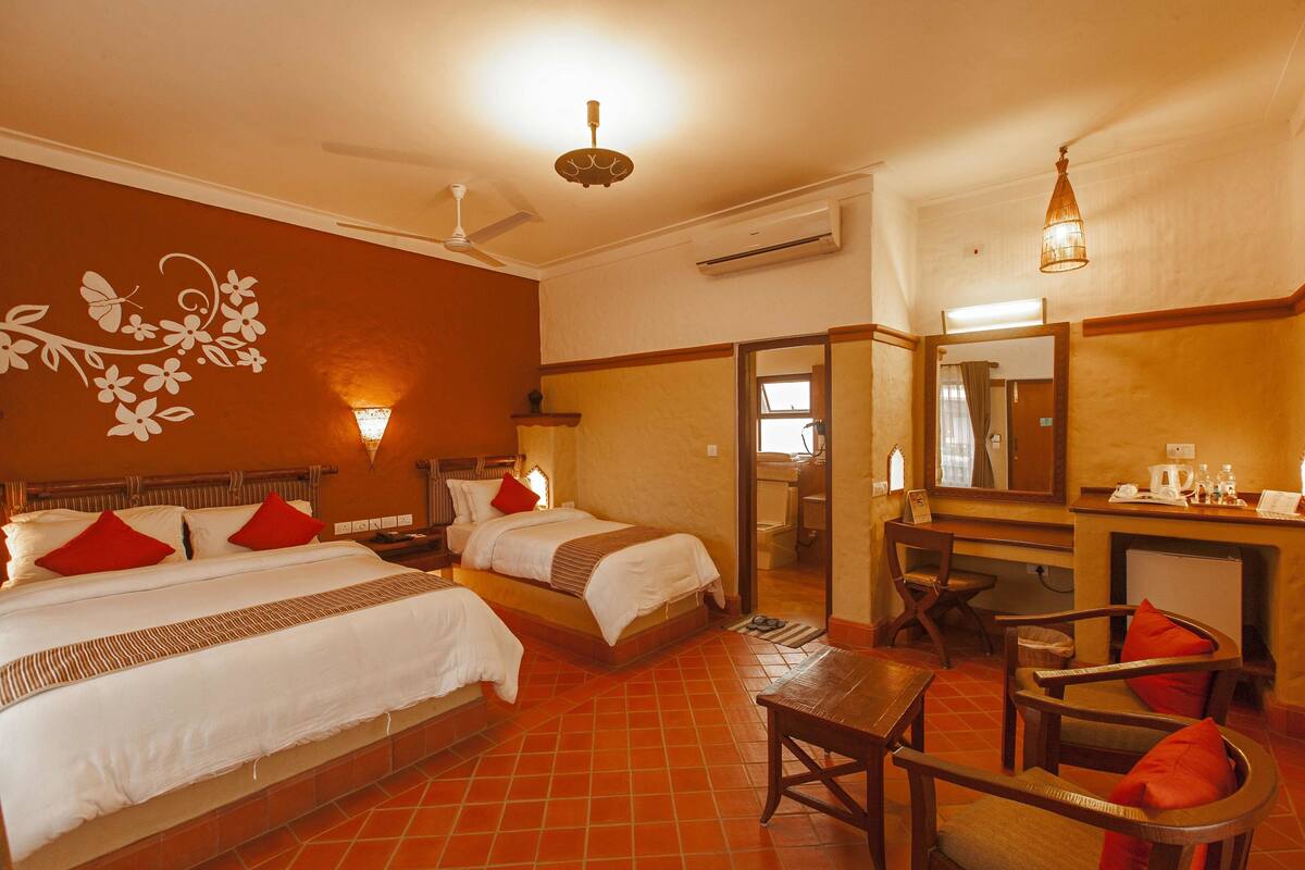A hotel room with two beds, a sitting area, a desk, and a mirror.