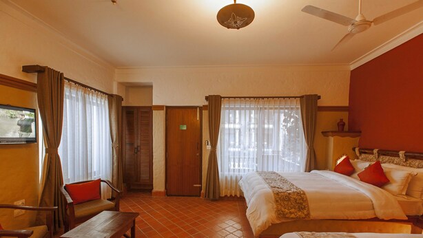A hotel room with two beds, a wooden desk, a chair, and a ceiling fan. - Green Park Chitwan (Sauraha)
