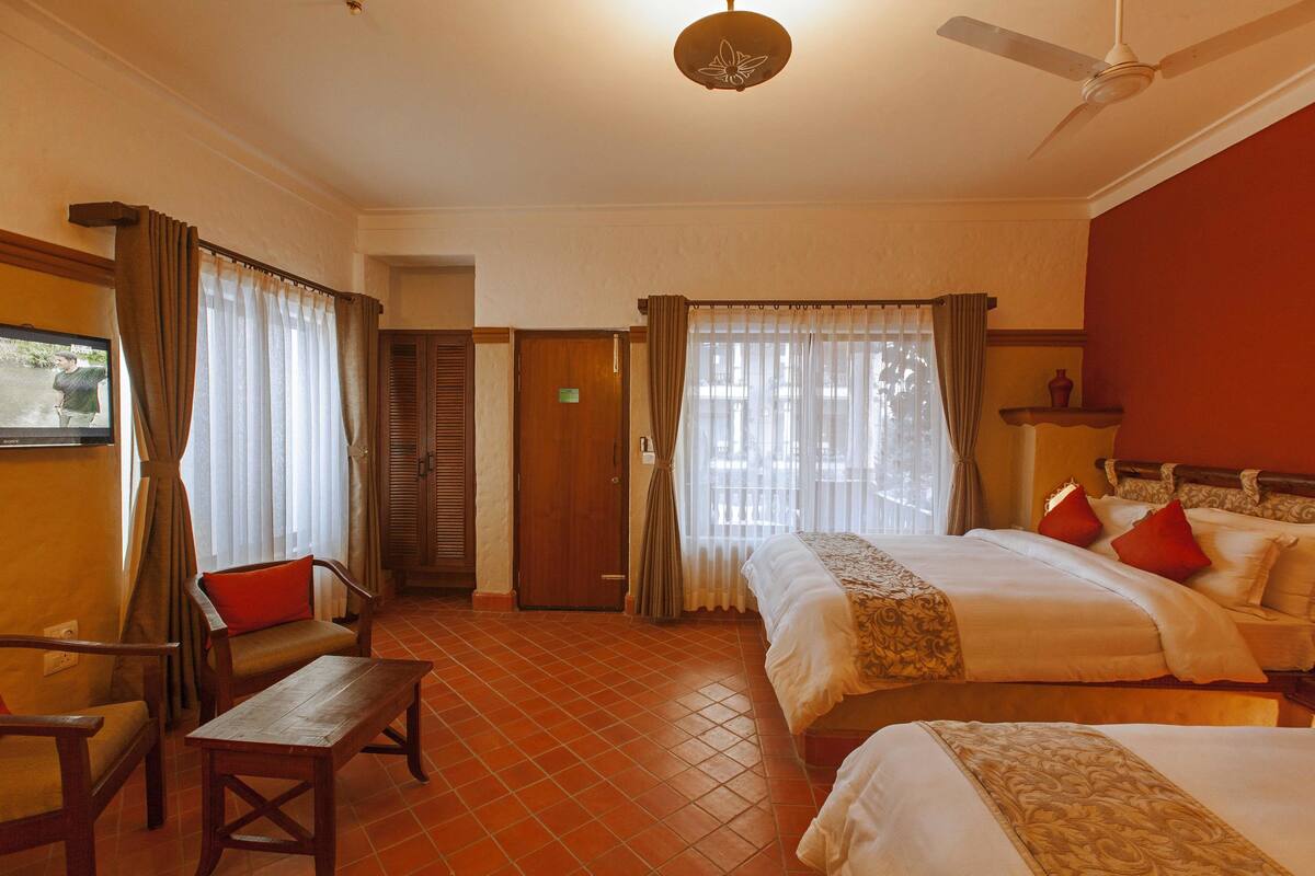 A hotel room with two beds, a wooden desk, a chair, and a ceiling fan.