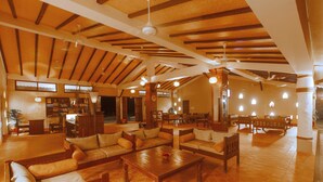 A spacious living area with wooden furniture, a fireplace, and a high ceiling with exposed beams. - Green Park Chitwan (Sauraha)