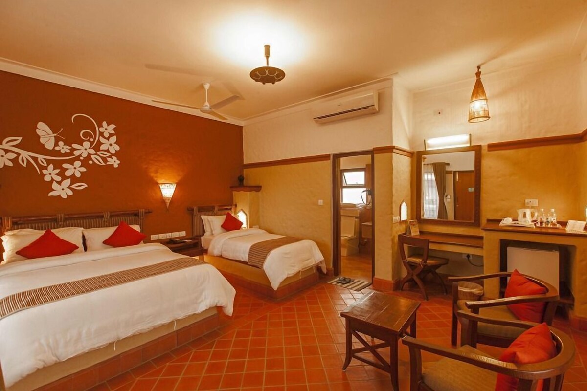 A hotel room with two beds, a desk, chairs, a mirror, and a ceiling fan.