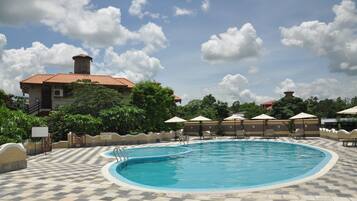 A swimming pool with a tiled deck, surrounded by umbrellas and trees.