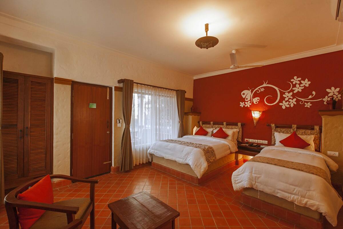 A hotel room with two beds, a wooden chair, a small table, and a decorative wall.