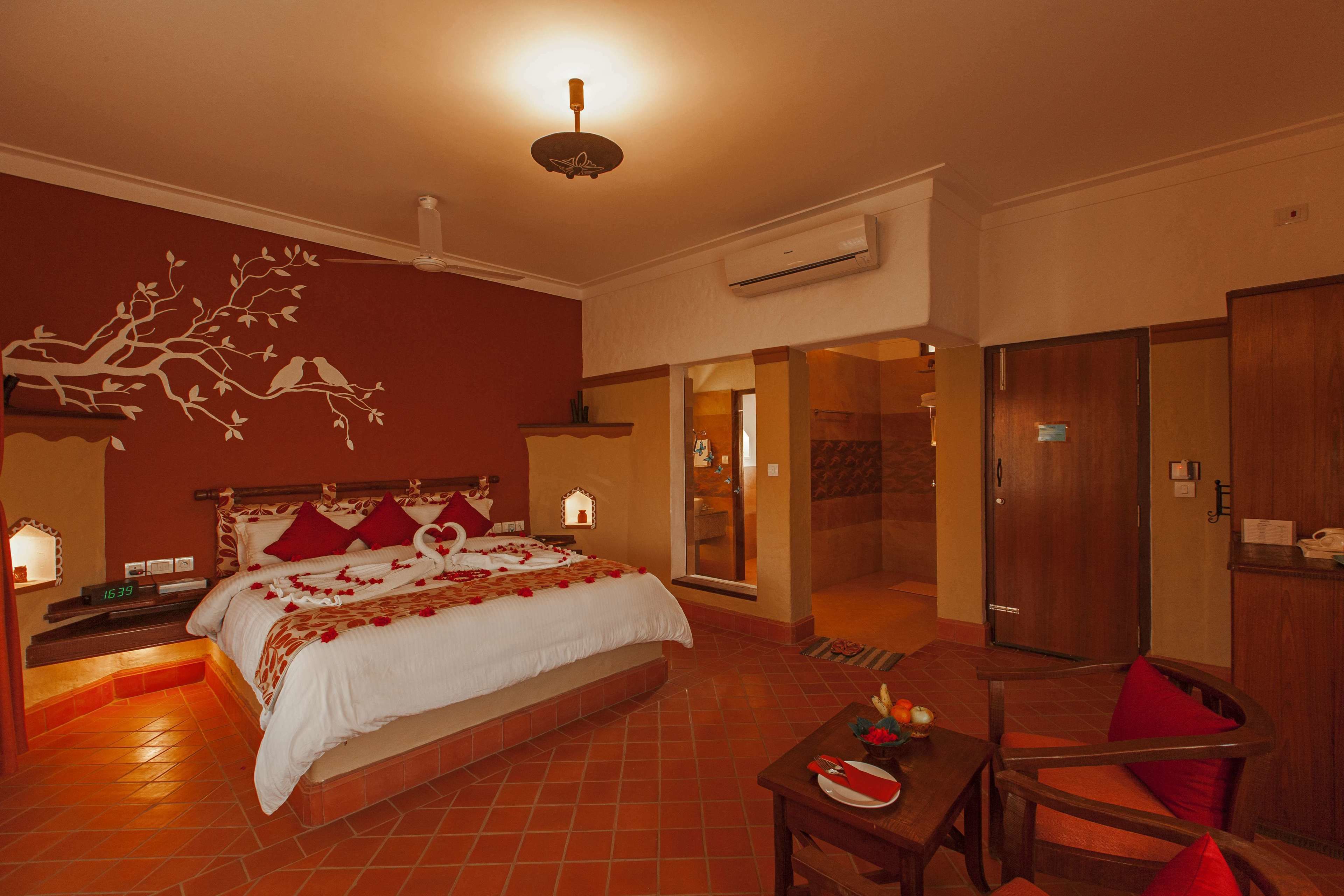 A hotel room with a large bed, a dining table with a plate of fruit, and a wooden chair.
