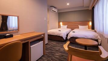 A hotel room with two beds, a desk, a chair, a small table, an air conditioning unit, and a mirror.