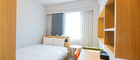 Una habitación de hotel con una cama grande, un escritorio, una silla, una mesita y una ventana con cortinas.