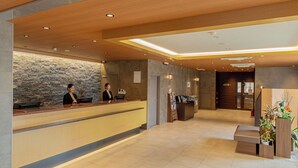 A reception area with a stone wall, a wooden reception desk, and a receptionist. - Central Hotel Takeo Onsen (Takeo)