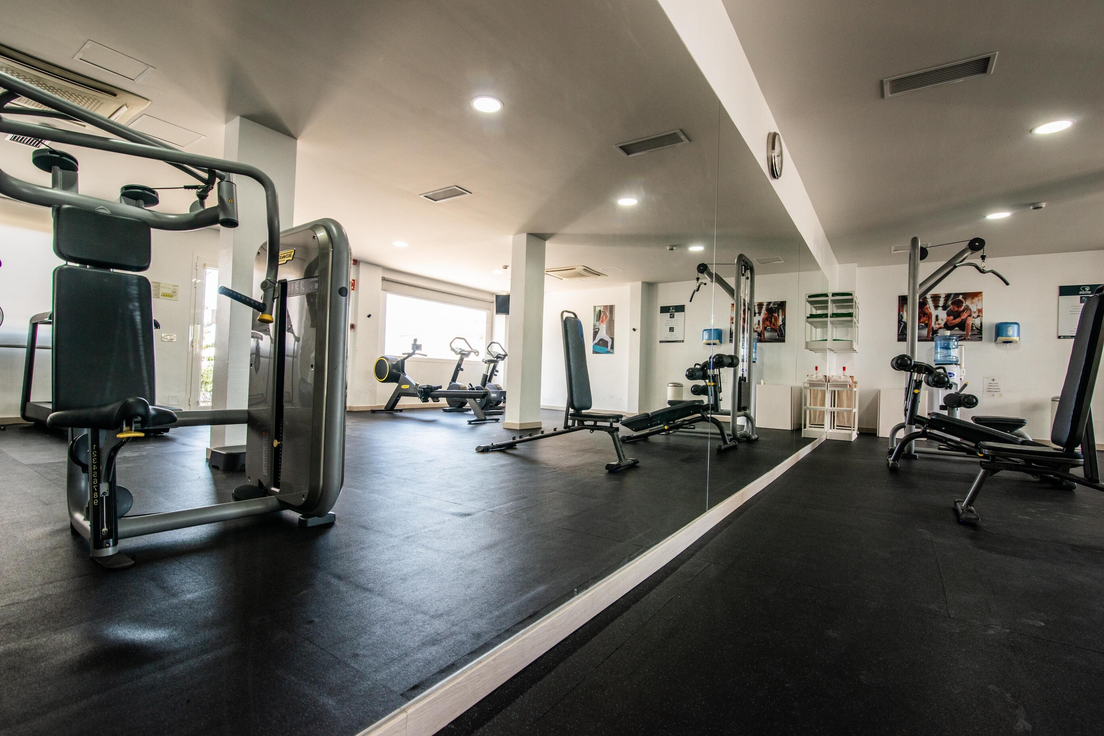 A gym with various exercise machines, a mirror, and a door leading to another room.