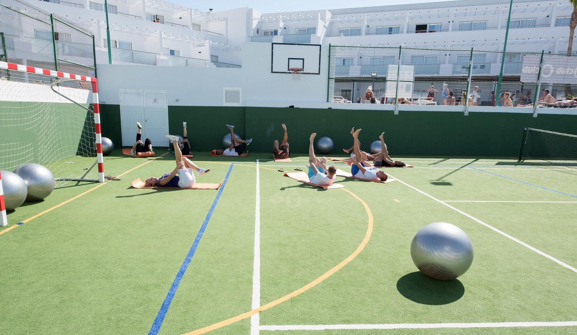 Une salle de sport en plein air équipée de tapis de sol, de grands ballons d’exercice et d’un panier de basket.