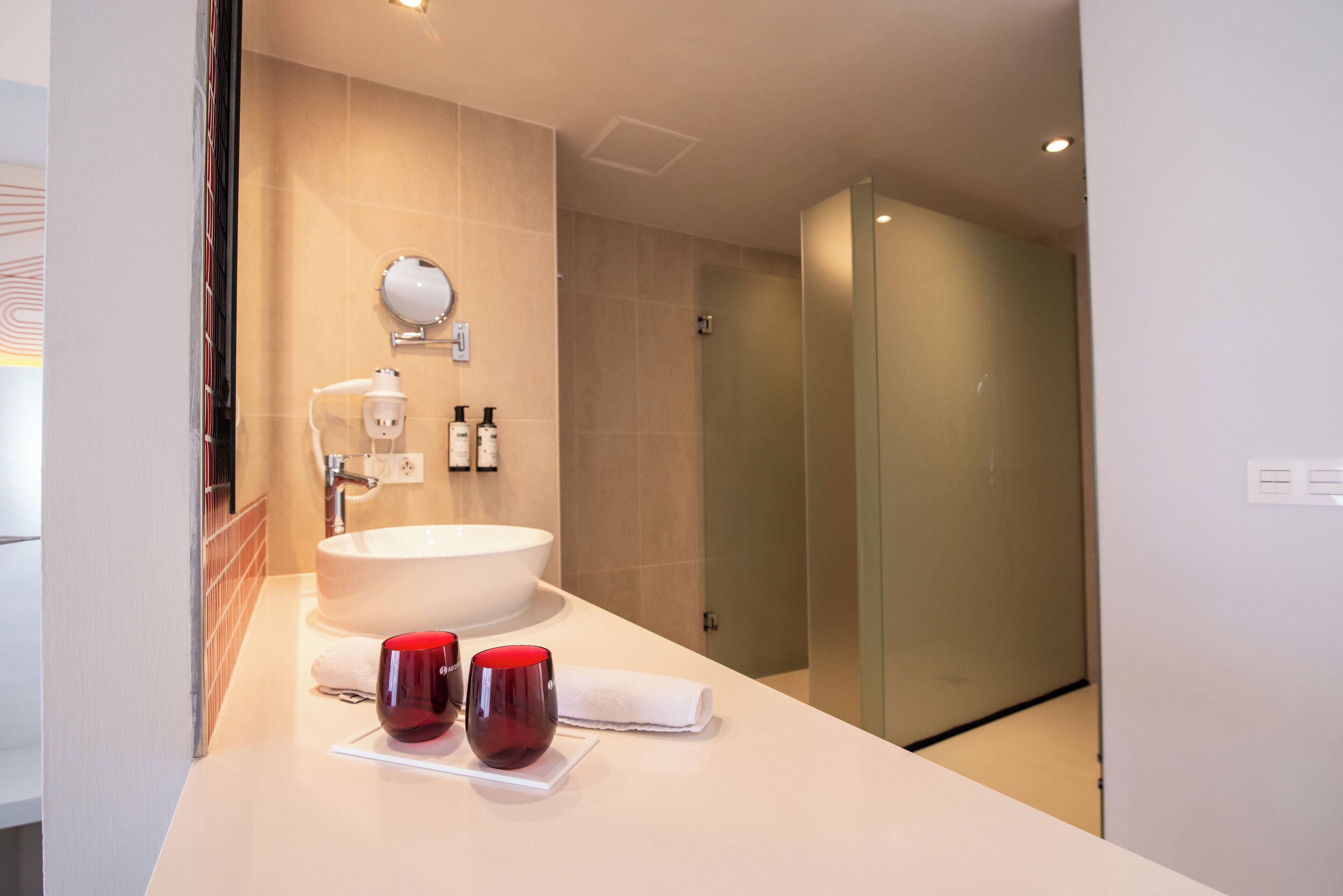 A modern bathroom with a large sink, a mirror, and two red cups on the counter.