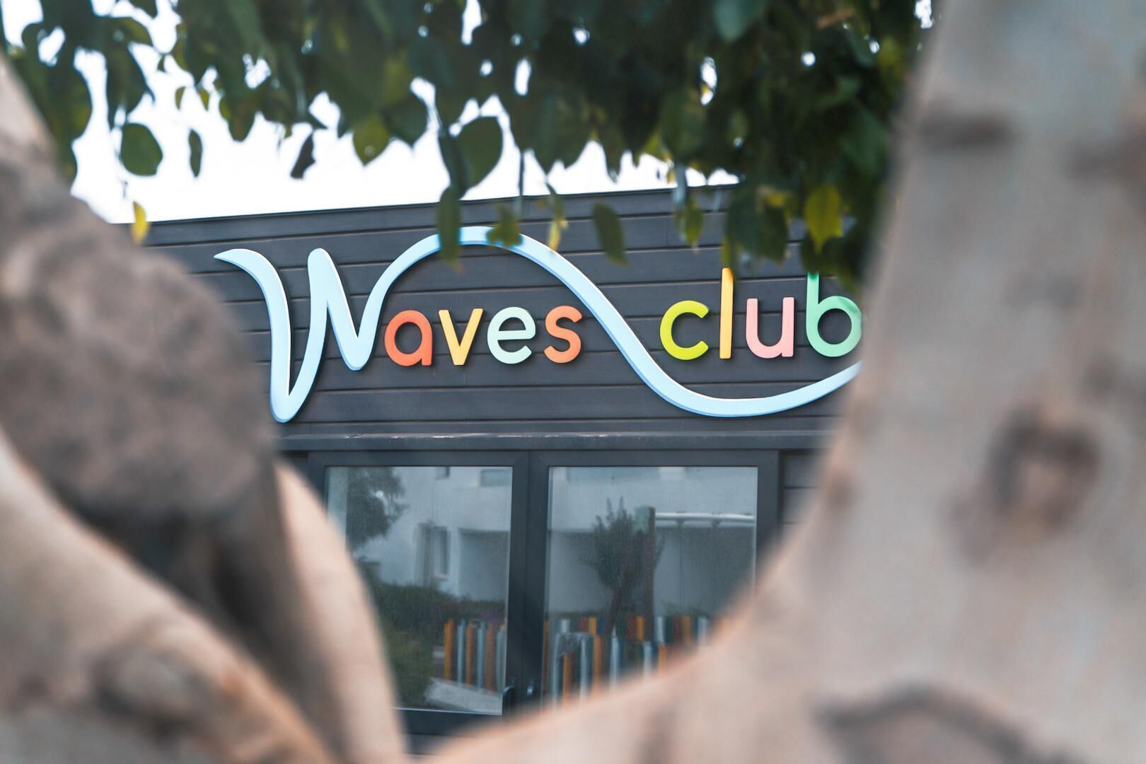 Cartell de Waves Club amb un disseny ondulat i lletres multicolores.